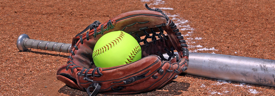 Softball resting in glove with bat on the field